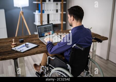 Businessman On Wheelchair While Working On Computer Stock Photo