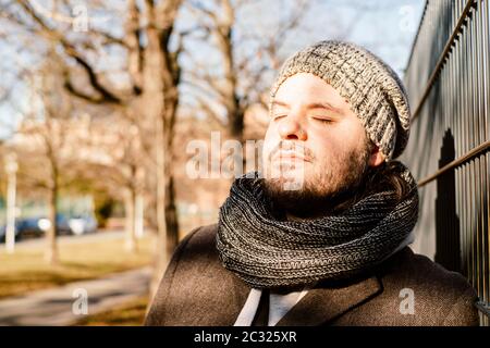 Man leans against a fence outside and enjoys the sun in the cold season. Contemplation, serenity and relaxing concept. Stock Photo