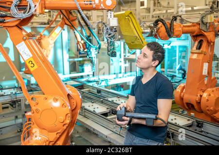 engineer controls using remote control of industrial robot in factory. Automatic welding and gluing using automation and robotic arms. Stock Photo