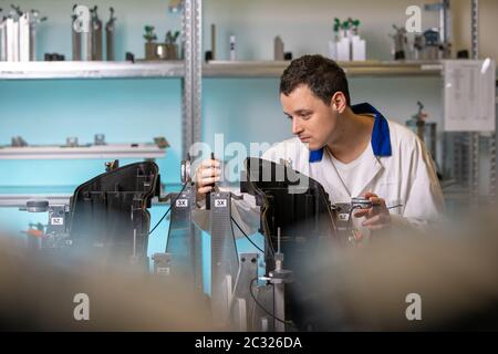 engineer measures plastic components for the production of lights for the automotive industry in a factory on a digital 3D machine. Stock Photo