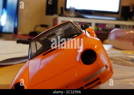 The process of assembling and painting the scale model of the car. Orange sports car in miniature. Installed front glass, mirror Stock Photo