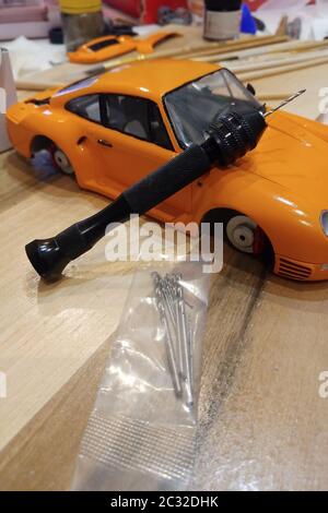 The process of assembling and painting the scale model of the car. Orange sports car in miniature. Manual mini drill. Stock Photo