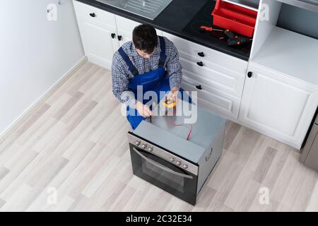 Young Male Technician Checking Oven With Digital Multimeter Stock Photo