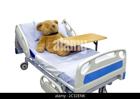 Brown teddy bear lying sick in bed with overbed table on body, isolated on white background, medical and healthcare concept Stock Photo