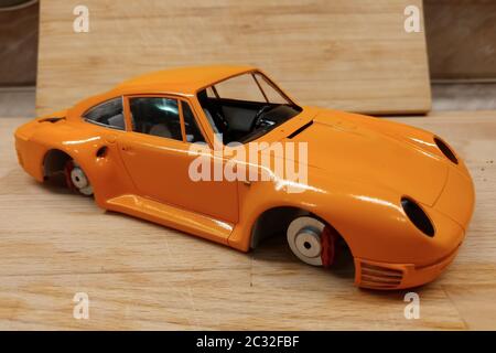 The process of assembling and painting the scale model of the car. Orange sports car in miniature. Stock Photo