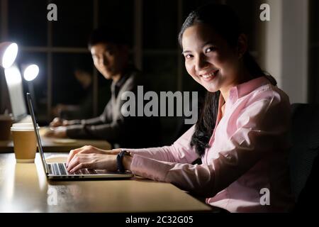 Young adult asian businessman and woman working late at night in their office with desktop computer and laptop. Using as hard working and working late Stock Photo