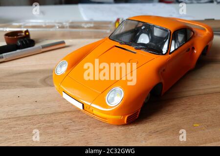 The process of assembling and painting the scale model of the car. Orange sports car in miniature. Installed front headlights windshield Stock Photo