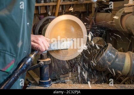 Making a wooden bowl on a lathe in an old small workshop with flying wooden shavings Stock Photo