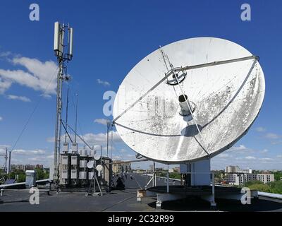 Huge retro satellite parabolic dish antenna on the roof for high speed internet link in front of blue sky Stock Photo