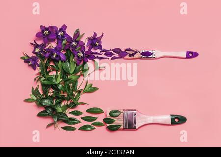 Colorful conceptual art background of paintbrush painting green leaves and violet flowers on pink backdrop. Spring and summer concept. Flat lay style. Stock Photo