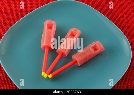 Red strawberry whistle lollipop sucker candy on blue plate on red tablecloth Stock Photo