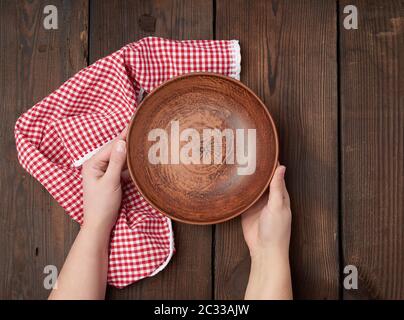 two female hands holding an empty round clay plate, top view Stock Photo
