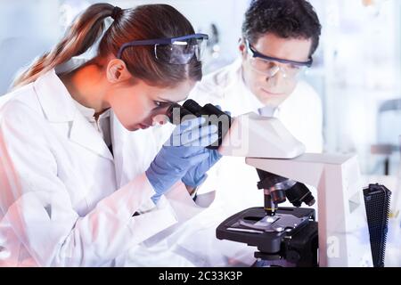 Life scientists researching in laboratory. Attractive female young scientist and her doctoral supervisor microscoping in their working environment. He Stock Photo