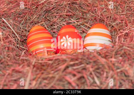 Traditional easter holiday festival celebration with three reddish eggs in hay straw in warm spring colors. Beautiful present symbol. Stock Photo
