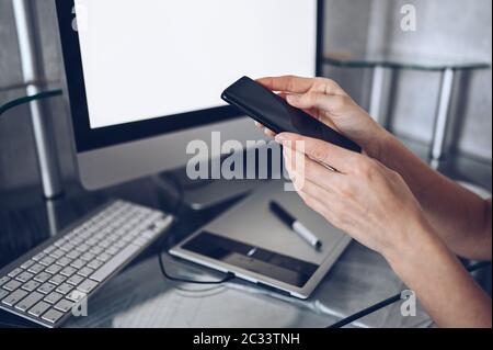 Female hands using smart phone in interior workplace, freelance business woman using cell phone at office desk, working from home using smart phone Stock Photo
