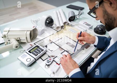 Architect Drawing Blueprint With Various Security Equipment On Desk Stock Photo