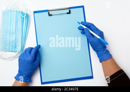 female hand in blue sterile gloves , on the table is a paper holder with clean blue sheets, top view Stock Photo