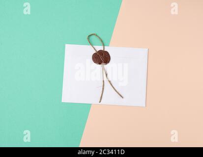 rectangular white paper envelope and brown stamp, color background, flat lay Stock Photo
