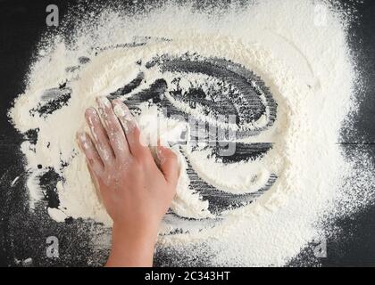 white wheat flour scattered on a black background, product is spread over the surface, kitchen background, top view Stock Photo