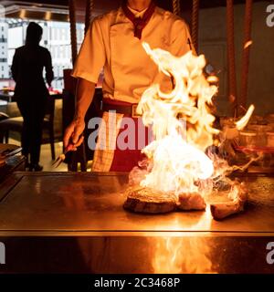 Cooking of beef teppanyaki recipe japanese grilled beef tomahawk steak on cooking pan using scraper with flame in background Stock Photo