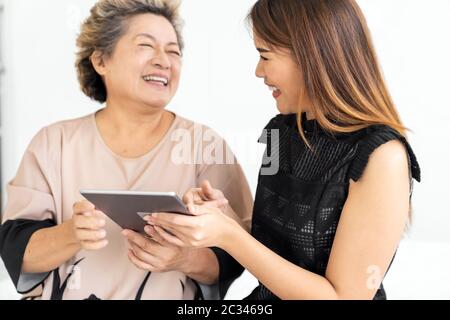 Cute young daughter teaching her happy old elderly mother to use digital tablet at home Stock Photo