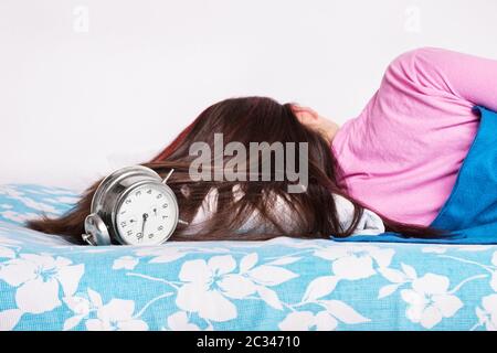 Beautiful young girl in pink pajamas calmly sleeping in her bed next to an old fashioned alarm clock, with her back turned to the camera. Healthy slee Stock Photo