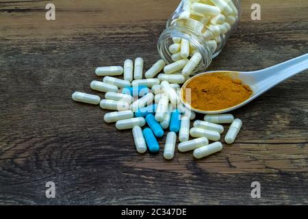 Colorful pill and yellow turmeric powder in ceramic spoon on grunge wooden background. Stock Photo