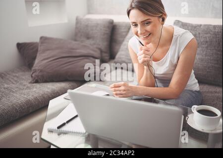 Attractive happy young student studying online at home, using laptop computer, headphones, having video chat, waving. Video conference or virtual Stock Photo
