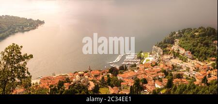 Mist over the Lake Maggiore, Laveno Mombello, Italy. Top View from Sasso del Ferro.  Church of Sant'Ambrogio and marina. Stock Photo