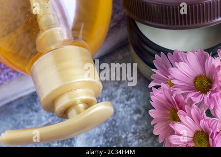 Shower gel in a large bottle and coconut oil for skin care. Presented in close-up next to chrysanthemum flowers. Stock Photo