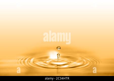 Closeup on drop of cosmetic golden oil liquid creating a circular wave. Stock Photo
