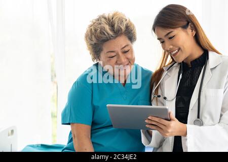 Asian confidence doctor using digital tablet expressing health concerns with old elderly woman patient sit on bed Stock Photo
