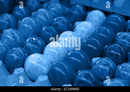 Close up many painted Easter chicken eggs in tray carton at retail display of farmers market, blue toned, high angle view Stock Photo