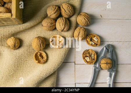 Walnuts in a wooden box, which stands on an old rustic sack, also scattered on a white table nearby is a cracker of walnut. Stock Photo