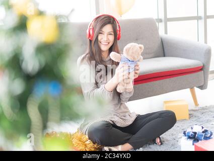 Beautiful Asian women smile happily. She is listening to the music on the red headphones. And holding a cute little teddy bear that she received as a Stock Photo