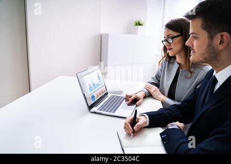 Two Businesspeople Analyzing Financial Graph On Laptop Stock Photo