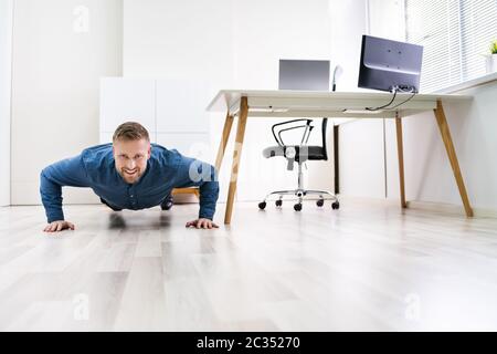 Businessman Doing Push Up On Hardwood Floor In Office Stock Photo