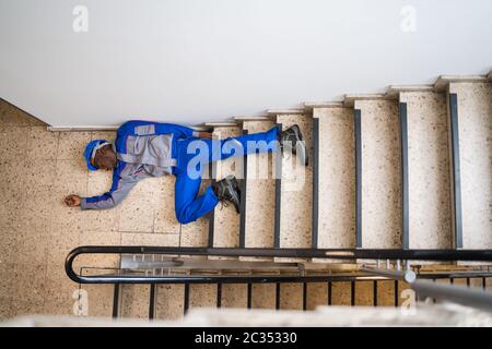 Unconscious Handyman Lying On Staircase With Helmet On Floor Stock Photo