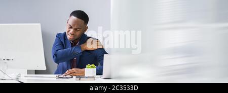 Young Businessman Having Shoulder Pain While Working At Computer Desk In Office Stock Photo