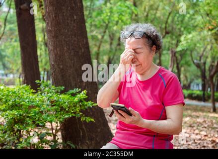 senior women have eye pain due to the use of mobile phones Stock Photo