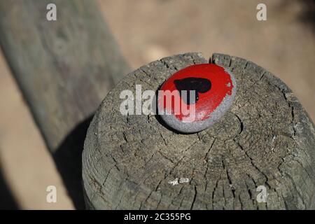 One small flat rock painted red, with a black heart, commemorating the BLM or Black Lives Matter movement. Was placed on a wooden fence post, sunlit. Stock Photo