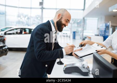 Man signs a contract to buy a new auto in car dealership. Customer and saleswoman in vehicle showroom, male person buying transport, automobile dealer