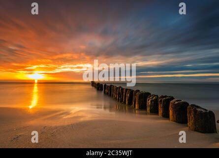 beautiful sunset on the Baltic Sea, waves washing the old wooden breakwaters Stock Photo