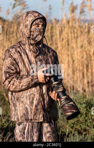 Naturalist photographer in action, with camouflage and camera, in the wilderness. Stock Photo