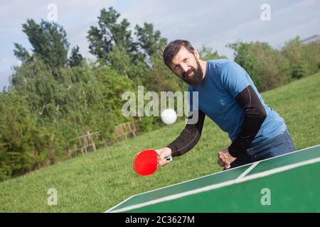 The bearded man is playing table tennis outdoors, active life concept. Stock Photo