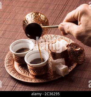 The male hand is pouring coffee in cup of coffee, copper Turkish coffee set. Stock Photo