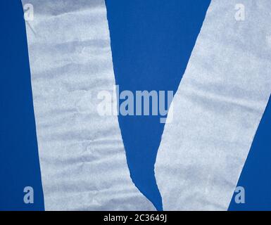 torn piece of white parchment paper on a blue background, close up Stock Photo