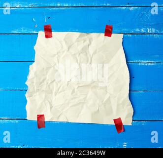 empty white crumpled sheet of paper glued with red sticky pieces of paper on a blue wooden background, place for text Stock Photo