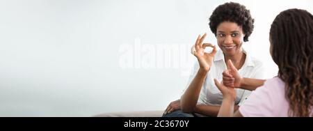 Portrait Of A Smiling African Young Woman Teaching Her Friend Hand Sign Language Stock Photo