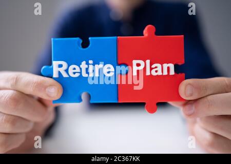 Overhead View Of Person's Hand Joining Plan And Retire Jigsaw Piece Stock Photo